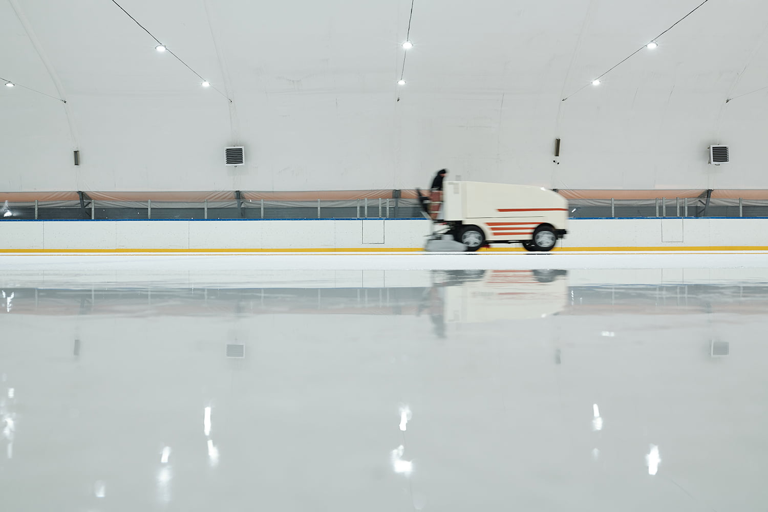 White truck or ice flattening machine moving along ice-rink while preparing it for playing hockey or skating inside large sports center